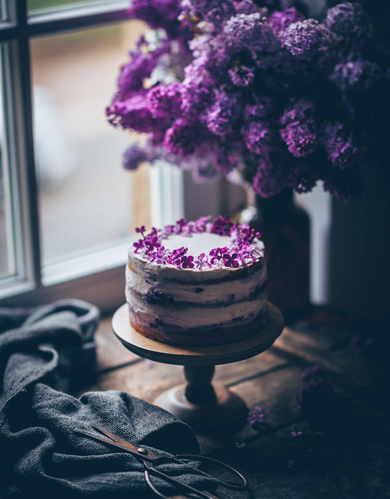 Fliederfarbener Kuchen mit Glasur und frischen Blüten