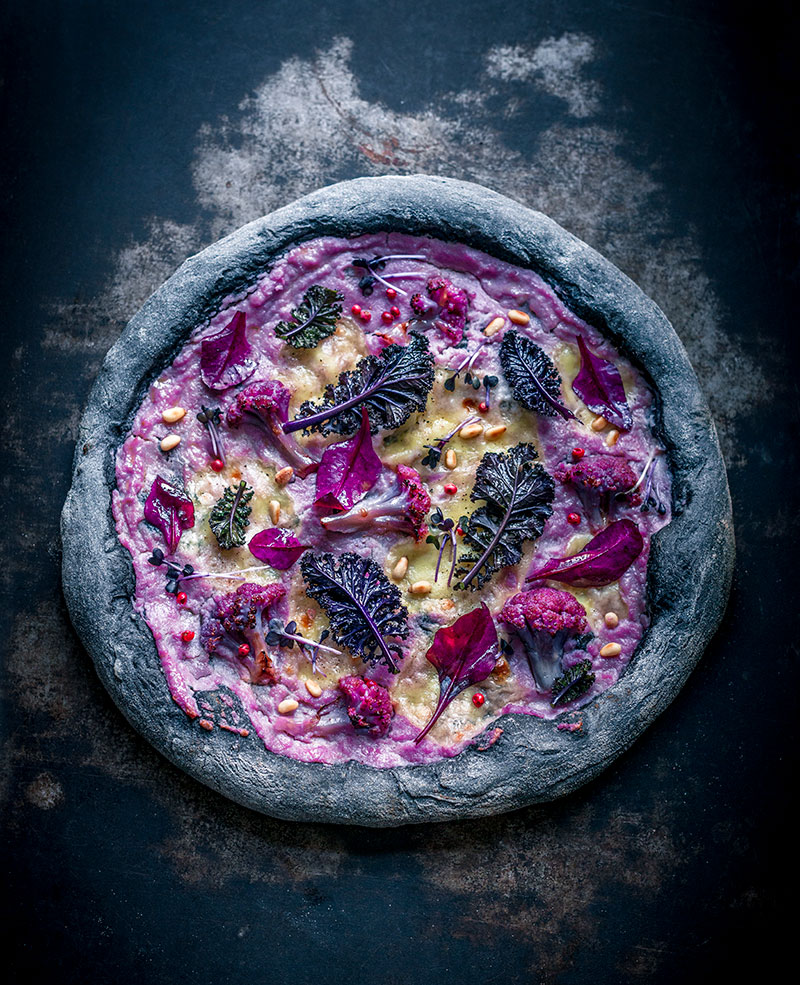 Lila Blumenkohl-Pizza mit bunten Toppings auf Backpapier